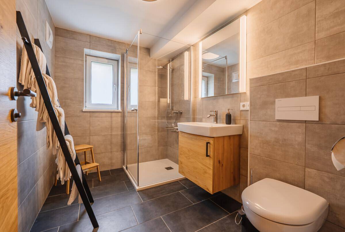 Modernes Badezimmer mit begehbarer Dusche, Waschtisch und Fenster für Tageslicht, in Grautönen gehalten.