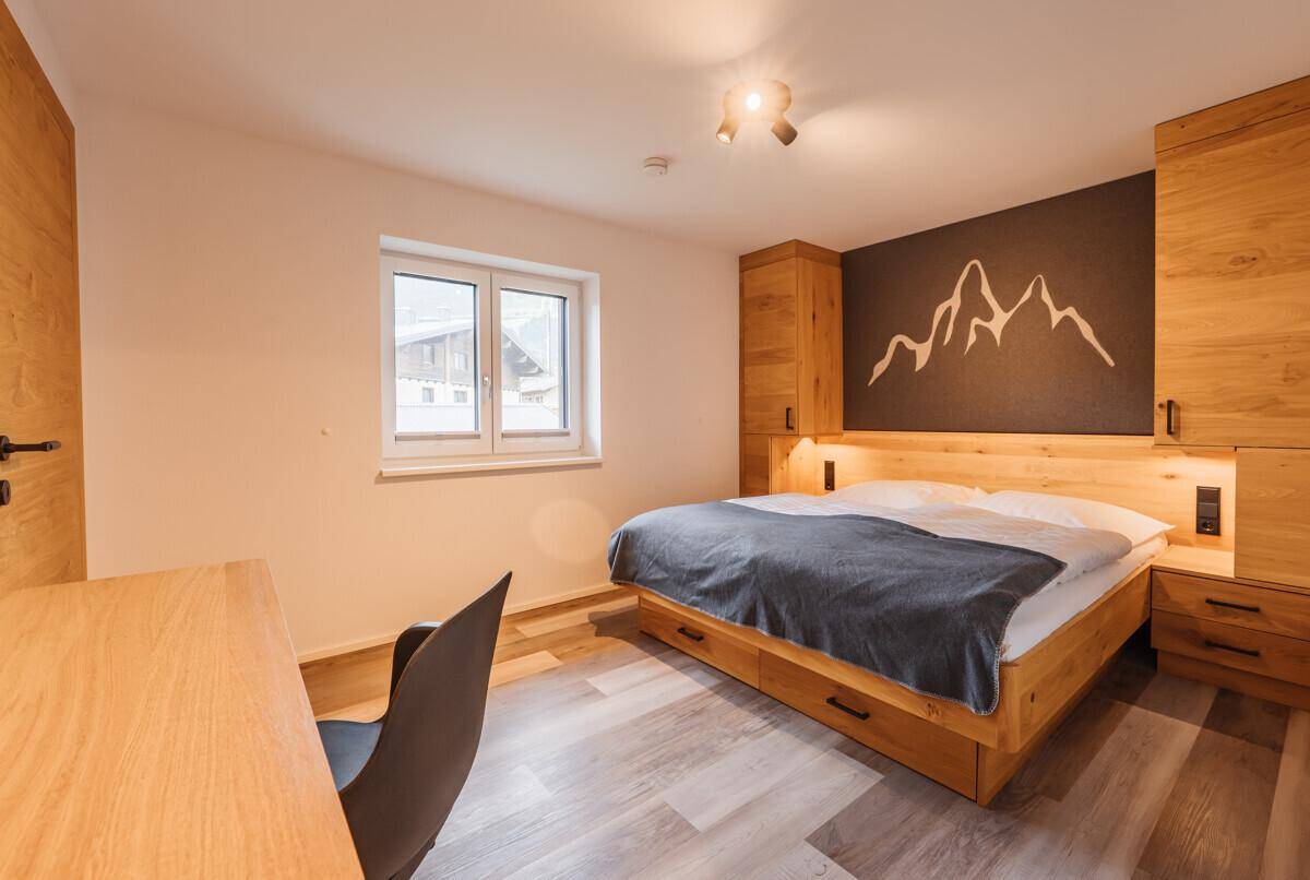 Helles Schlafzimmer mit Holzbett, Schreibtisch und Fenster mit Blick nach draußen, modern eingerichtet.