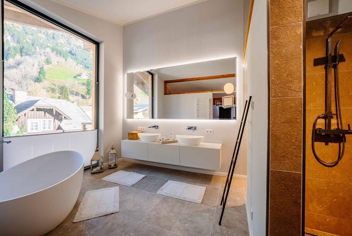 Luxuriöses Badezimmer mit freistehender Badewanne, Doppelwaschbecken und großem Fenster mit Bergblick.