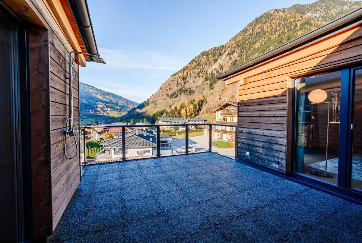 Geräumige Terrasse mit Glasgeländer, Außendusche und Blick auf die umliegende Berglandschaft.