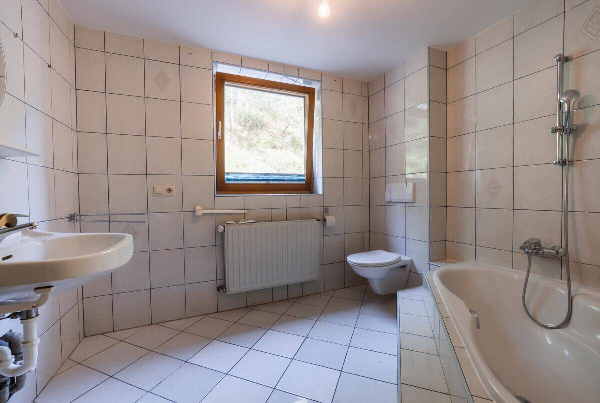 Badezimmer im älteren Stil mit weißen Fliesen, Badewanne, WC und Fenster.