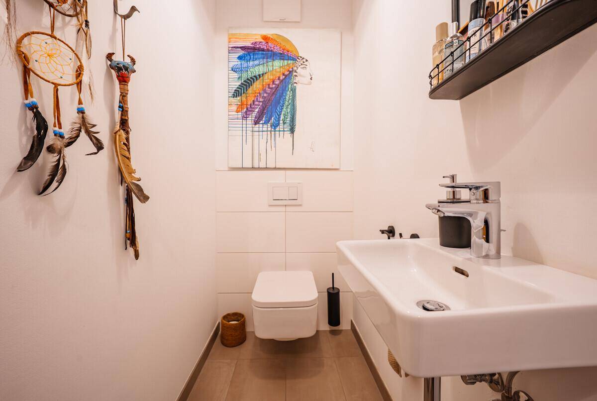 Gäste-WC mit wandhängender Toilette und Waschbecken, farbenfroh dekoriert mit einem Gemälde.