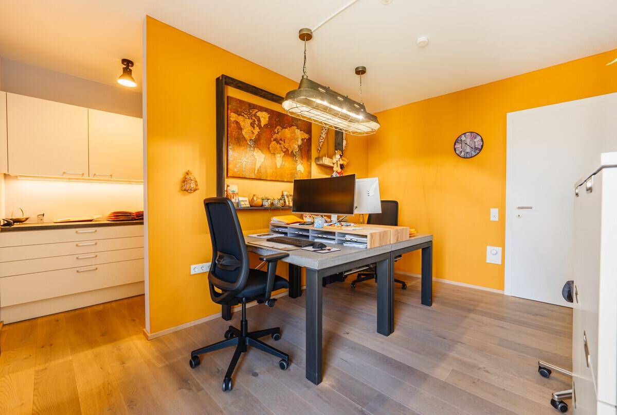 Funktionaler Arbeitsbereich mit Schreibtisch und orangefarbener Wand, angrenzend an die Küchenzeile.