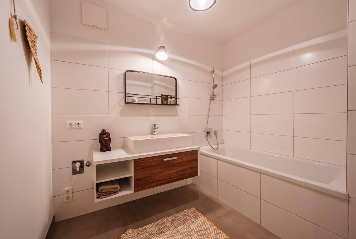 Modernes Badezimmer mit Badewanne, schwebendem Waschtisch und weißen Fliesen, hell und funktional gestaltet.