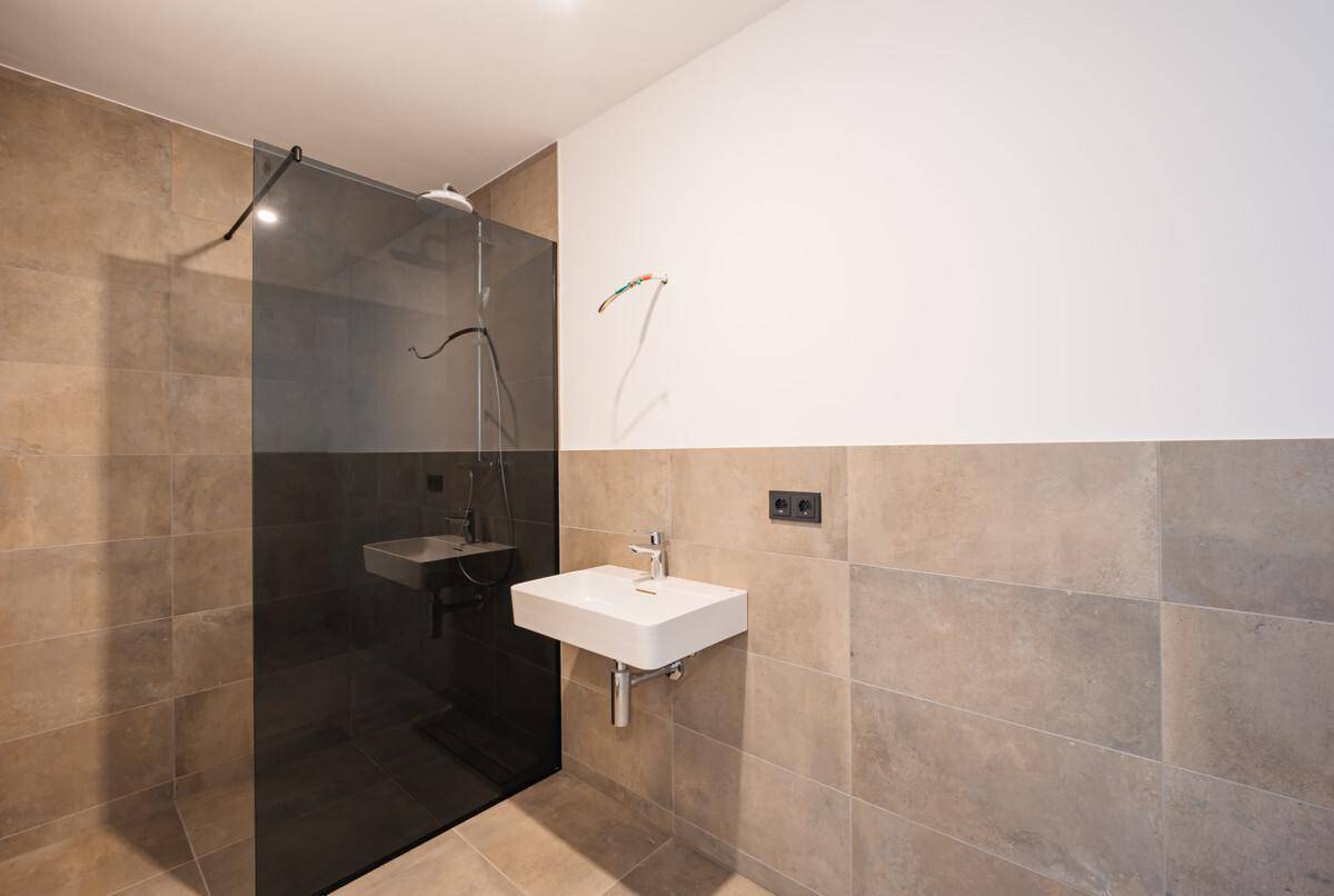Modernes Badezimmer mit begehbarer Dusche, Einzelwaschbecken und beigefarbenen Fliesen.