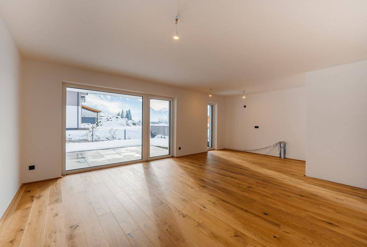 Geräumiges, unmöbliertes Wohnzimmer mit hellen Wänden und robustem Holzdielenboden.