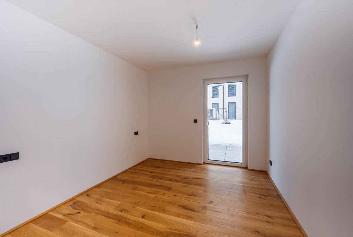Kleineres, helles Zimmer mit Holzdielenboden und Zugang zu einem Außenbereich.