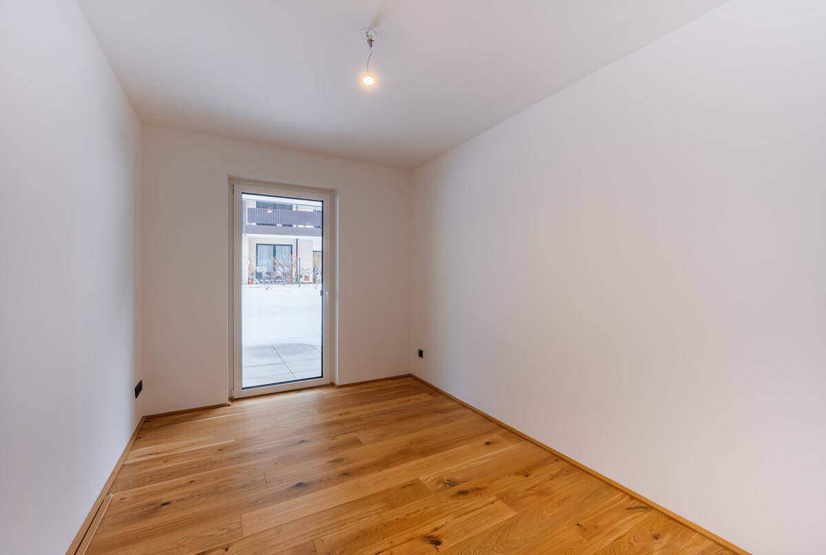 Unmöbliertes Zimmer mit weiß gestrichenen Wänden und warmem Holzdielenboden.