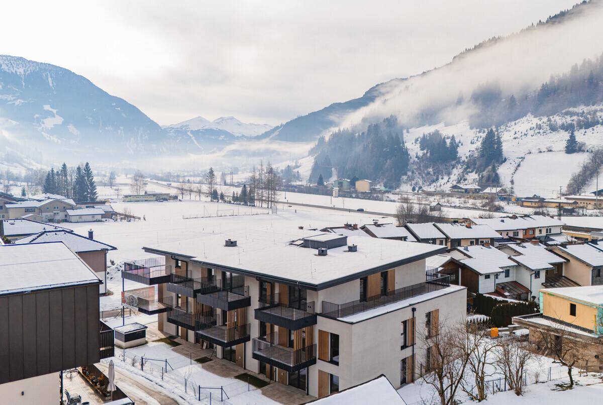 Modernes Apartmentgebäude in verschneiter Winterlandschaft mit nebelverhangenen Bergen und Balkonen.