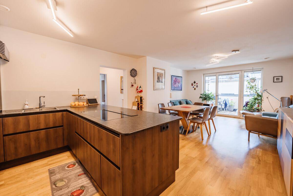 Offener Wohn-Essbereich mit moderner Holzküche, Parkettboden und Zugang zur Terrasse.