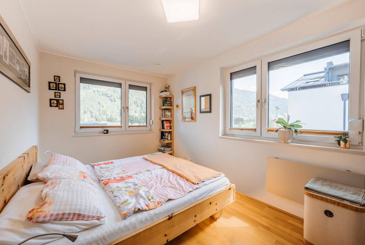 Helles Schlafzimmer mit Holzbett, Parkettboden und Fenstern mit Blick auf die Berge.