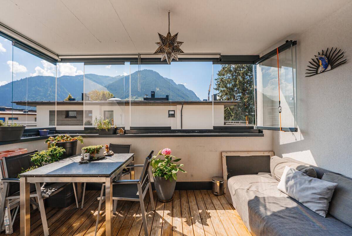 Verglaster Balkon mit Holzboden, Sitzgelegenheiten und Panoramablick auf die Berge.