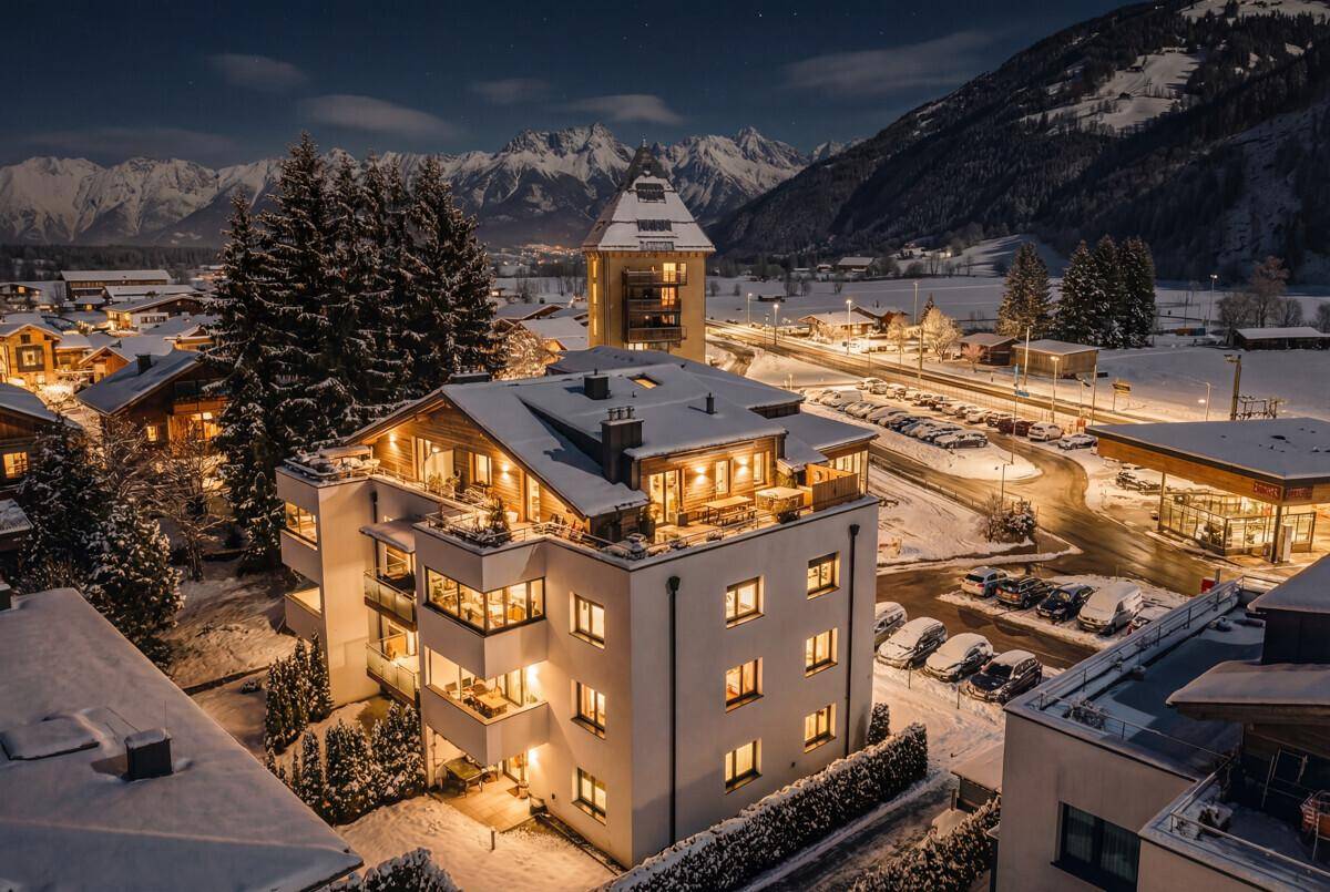 Beleuchtetes Wohngebäude bei Nacht in einer verschneiten Berglandschaft.
