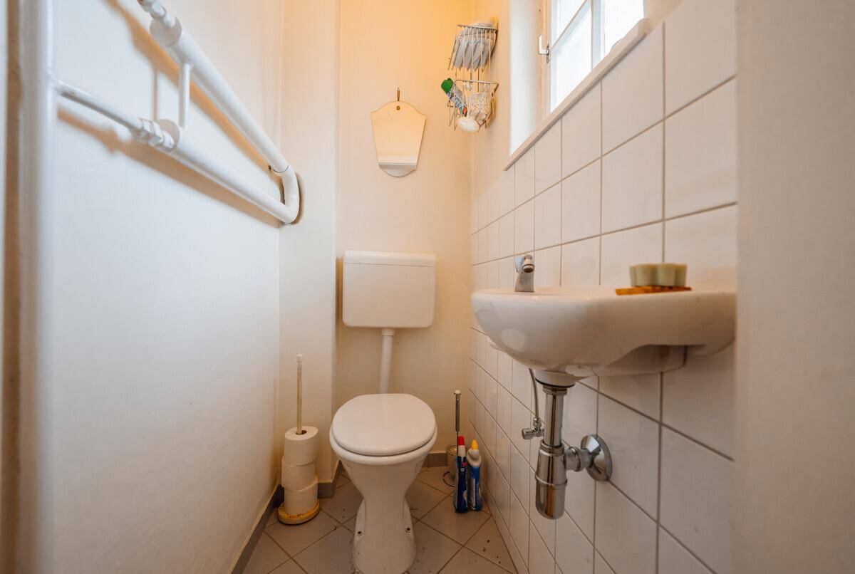 Kleines Gäste-WC mit Fenster, Toilette und Waschbecken, ausgestattet mit weißen Fliesen.