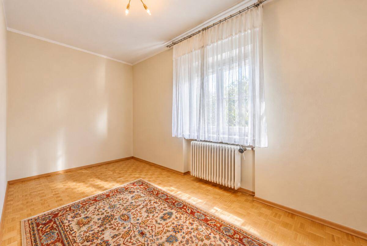 Helles Zimmer mit Parkettboden, großem Fenster und einem traditionellen Teppich.