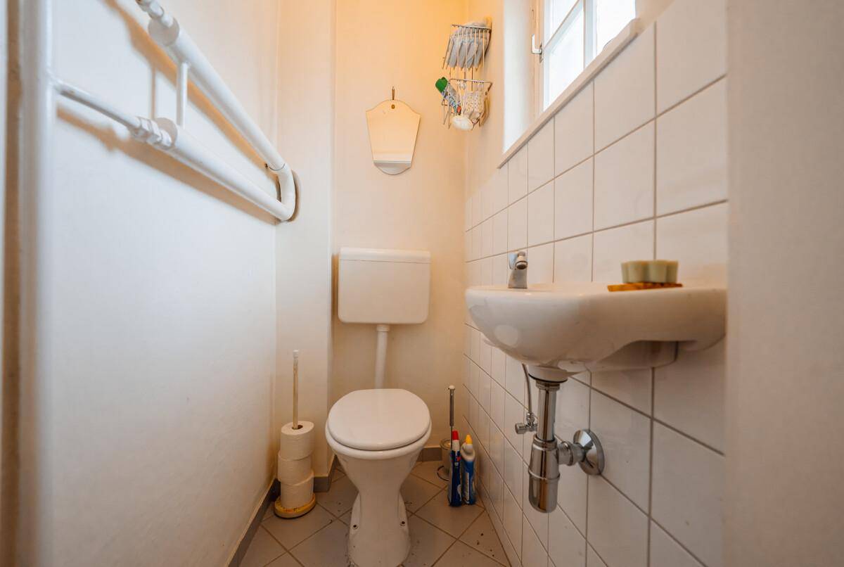 Kleines Gäste-WC mit Fliesenboden, Fenster und einem Wandheizkörper.