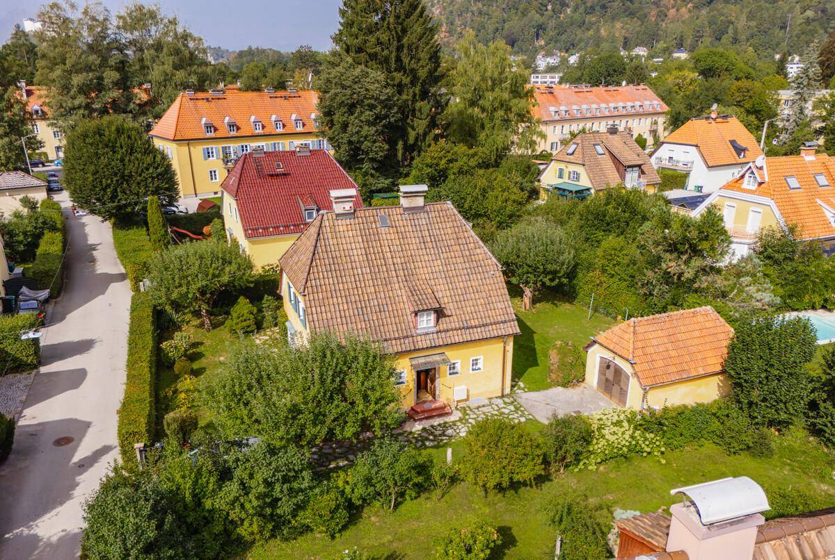 Übersicht über ein gelbes Einfamilienhaus mit Ziegeldach, umgeben von gepflegten Gärten und Bäumen.