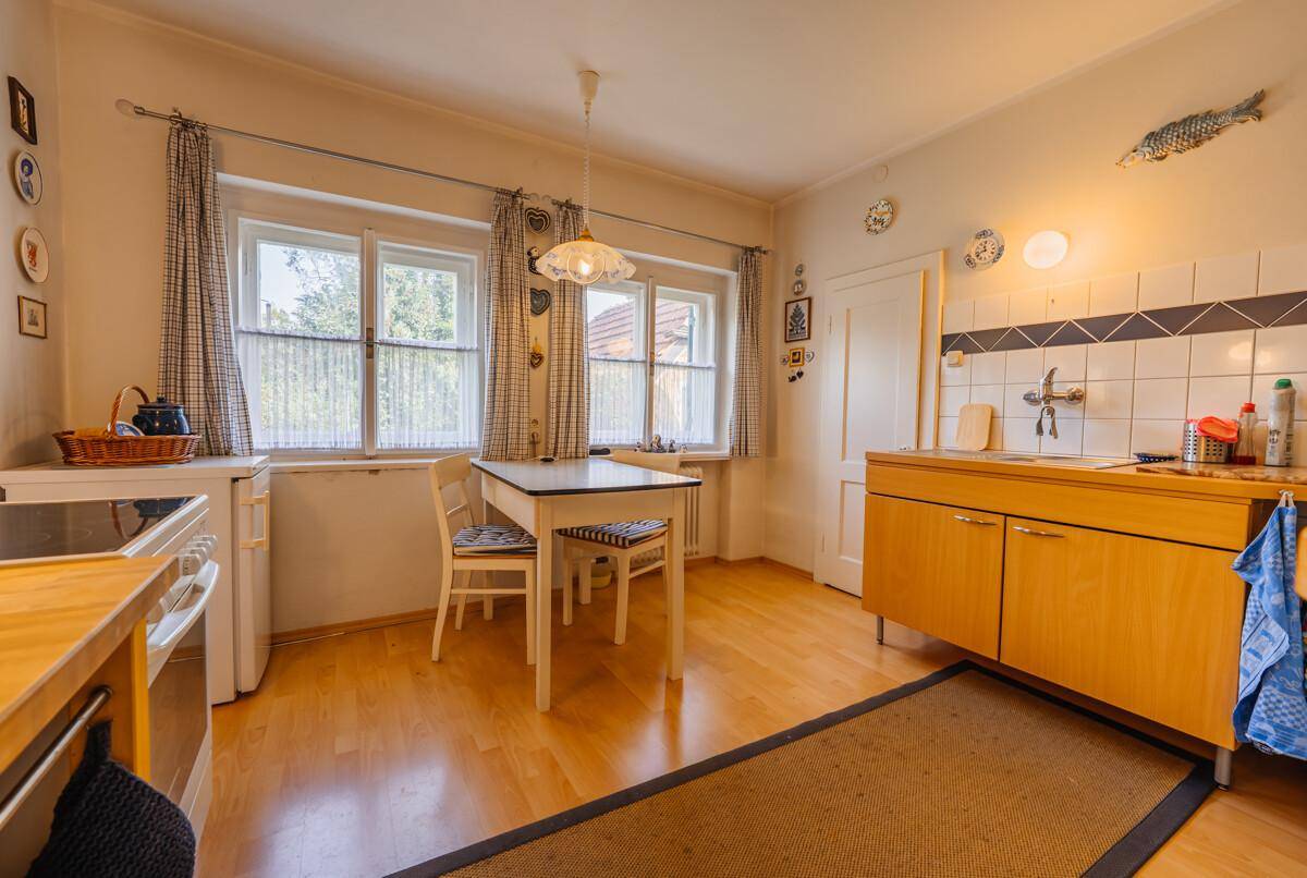 Helle Küche mit Holzboden, Esstisch und Blick in den Garten durch zwei Fenster.