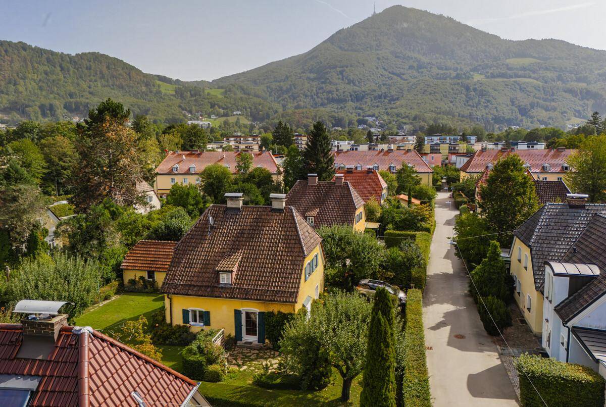 Panoramablick auf ein gelbes Haus mit Ziegeldach, umgeben von viel Grün und einer ruhigen Straße.