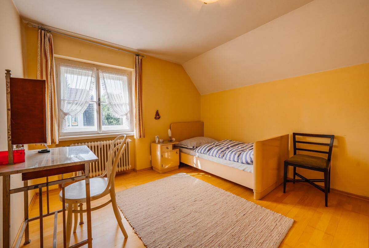 Schlafzimmer mit gelben Wänden, Holzboden und einem Einzelbett neben einem Fenster.