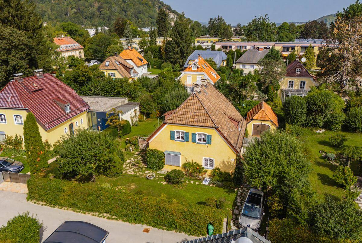 Vogelperspektive eines traditionellen gelben Hauses mit großem Garten und umgebenden Wohnhäusern.