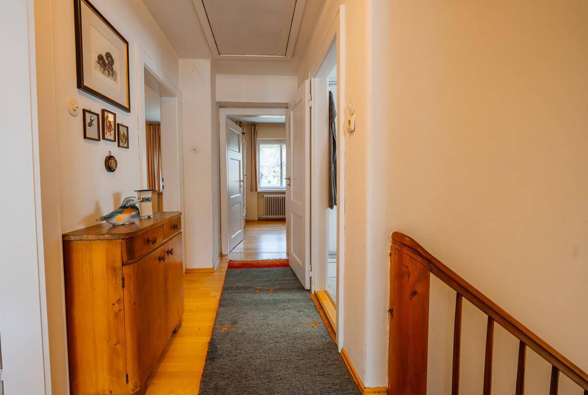 Heller Flur mit Holztreppe, Parkettboden und Zugang zu weiteren Zimmern.