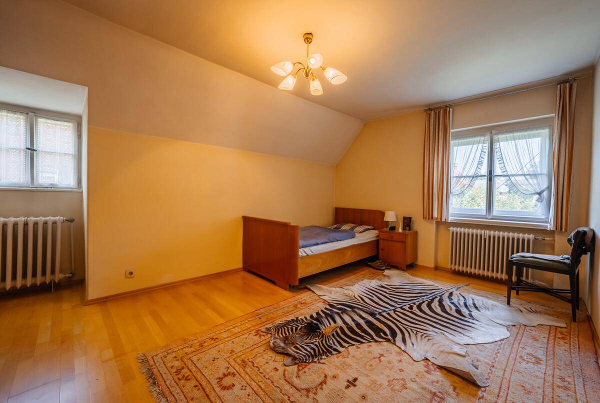 Geräumiges Schlafzimmer mit Holzboden, zwei Fenstern und einem dekorativen Teppich.