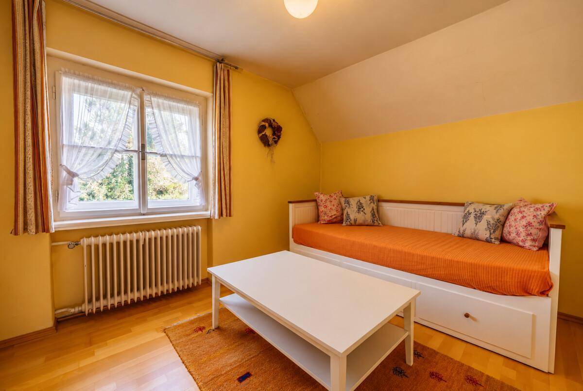 Gemütliches Schlafzimmer mit gelben Wänden, Holzboden und einem Tagesbett.
