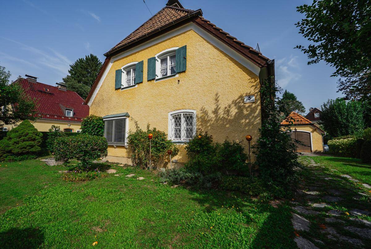 Charmantes gelbes Haus mit Ziegeldach, grünen Fensterläden und einem gepflegten Vorgarten.