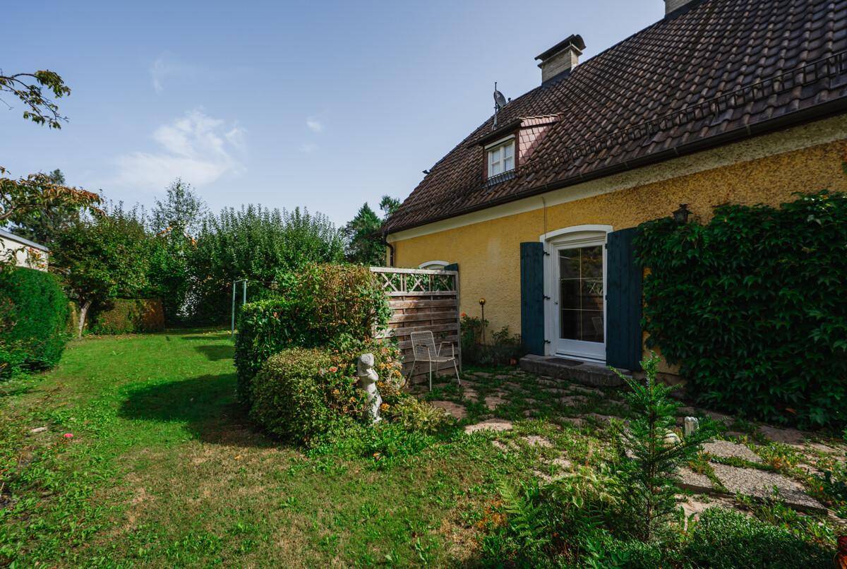 Sonniger Gartenbereich mit Rasen, Hecken und einem kleinen Sitzplatz neben dem Haus.