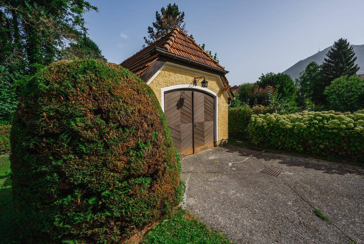 Traditionelle Garage mit Holztüren und Ziegeldach, umgeben von gepflegten Hecken.
