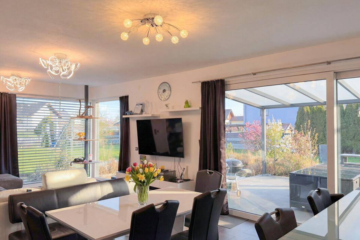 Heller Wohn- und Essbereich mit großen Fensterfronten und Zugang zur überdachten Terrasse.