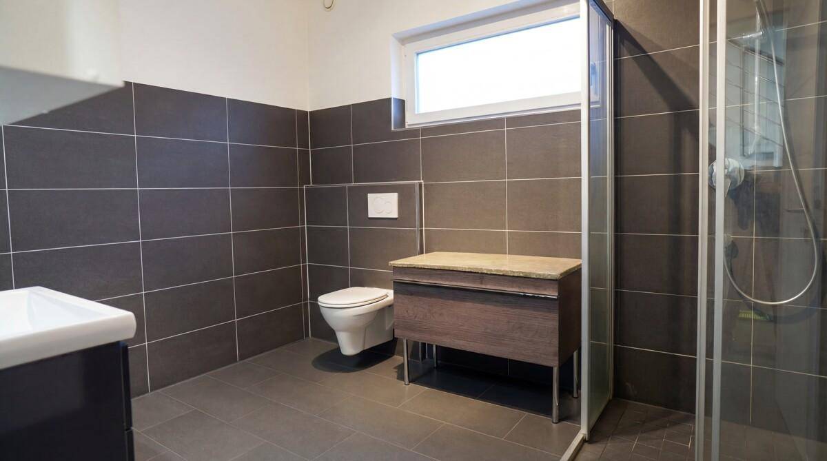 Geräumiges Badezimmer mit Dusche, WC, Waschtisch und Fenster für natürliche Belüftung.