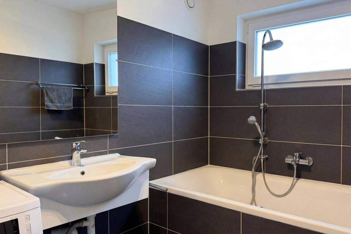 Modernes Badezimmer mit Badewanne, Dusche, Einzelwaschbecken und Fenster für Tageslicht.