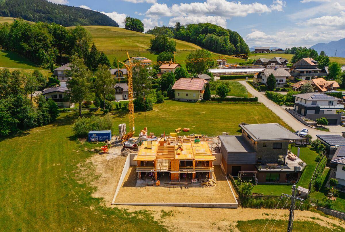 Baustelle eines Neubaus mit Kran und Holzrohbau, eingebettet in eine ländliche Wohngegend.