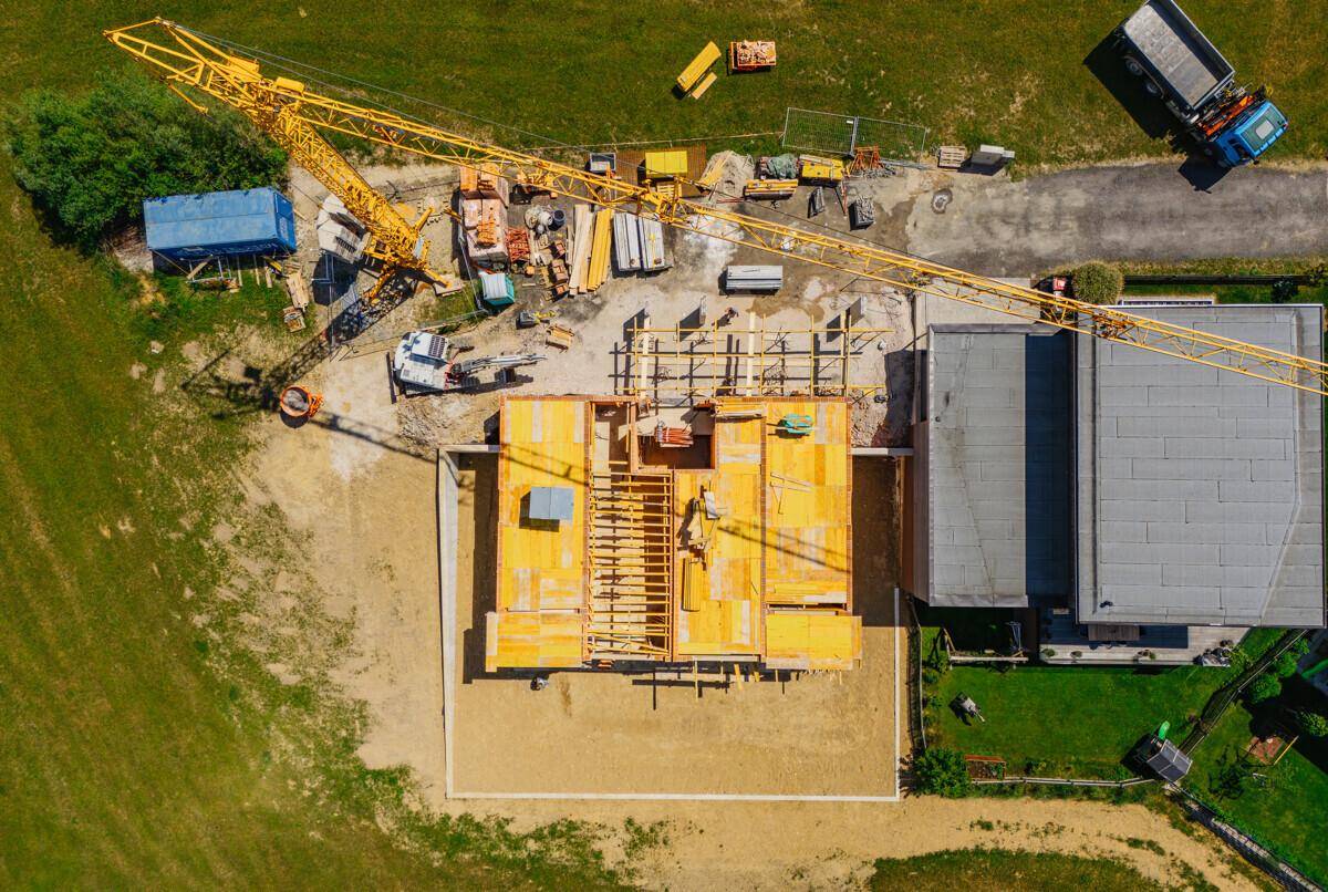 Vogelperspektive einer Baustelle mit Kran und dem Fundament eines im Bau befindlichen Hauses.