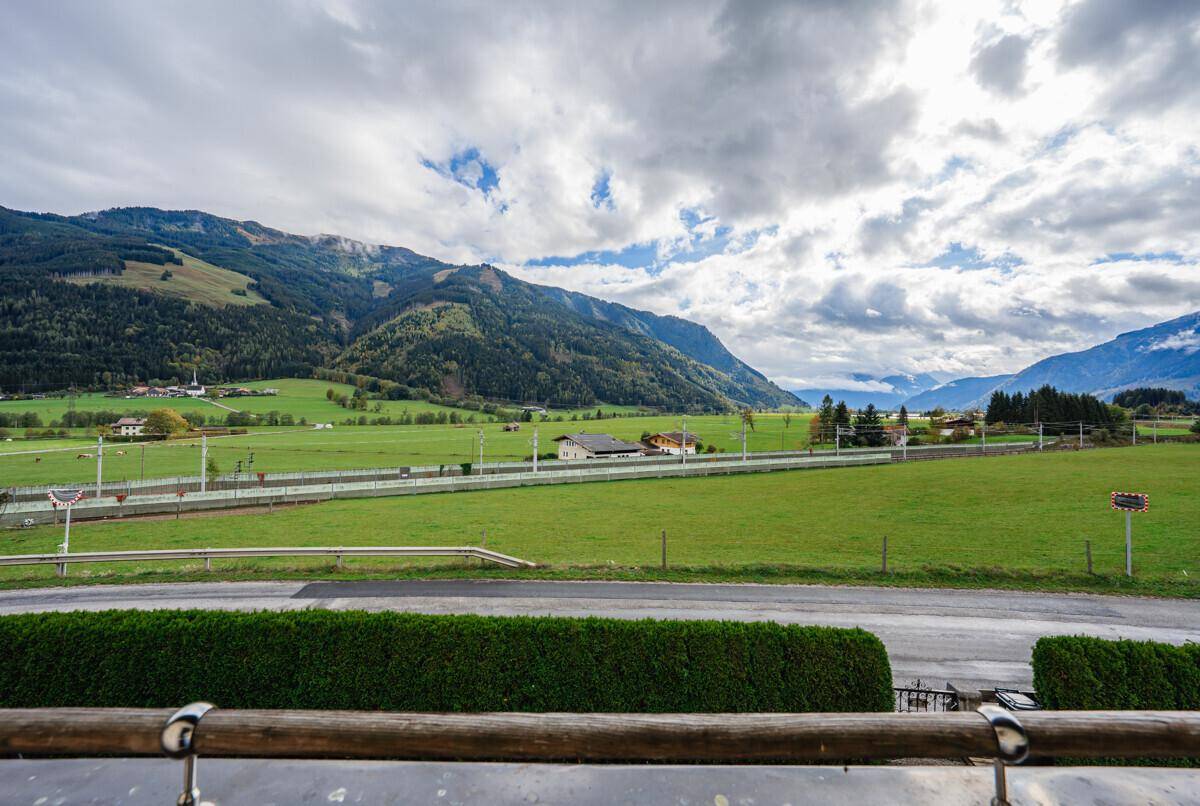 Weitläufiger Blick auf grüne Felder und majestätische Berge unter einem bewölkten Himmel.