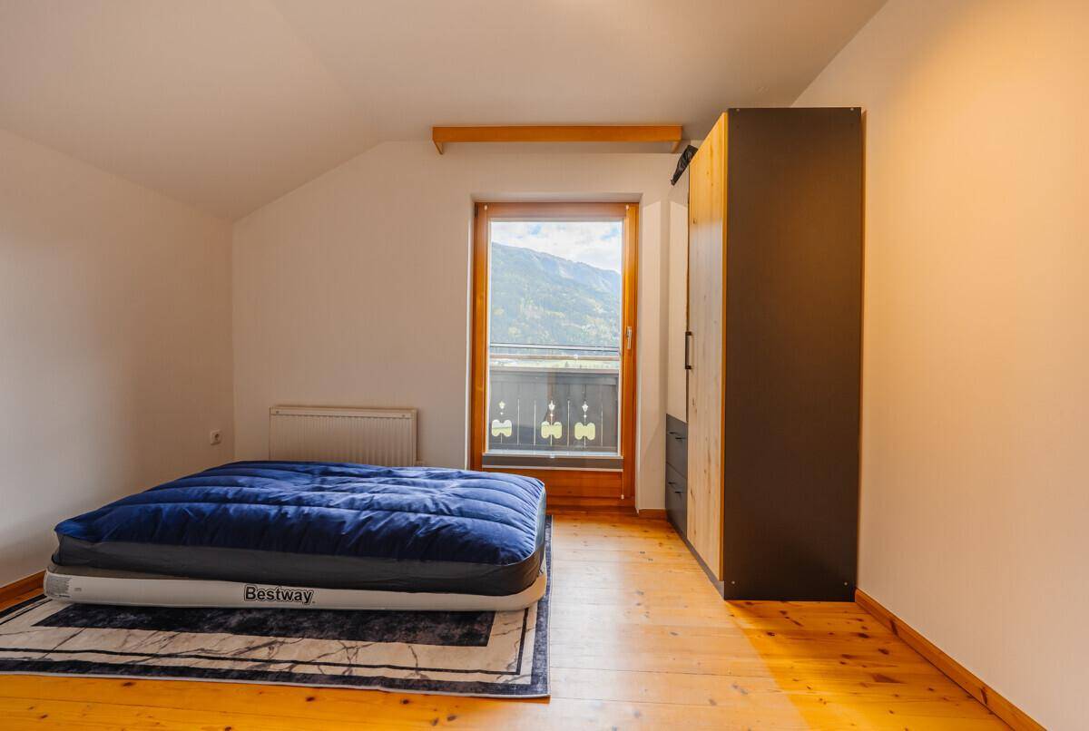Gemütliches Schlafzimmer mit Holzboden, Kleiderschrank und Balkontür mit Bergblick.