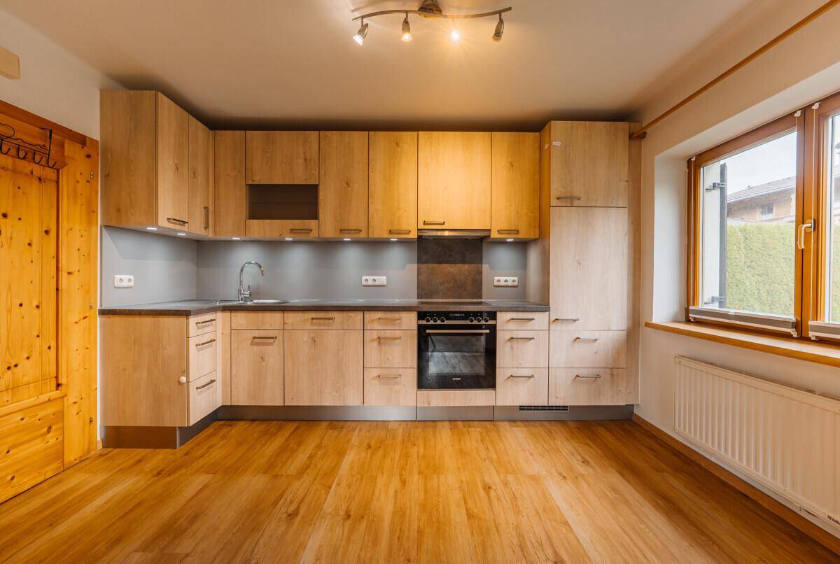 Moderne Einbauküche mit hellen Holzfronten, integrierten Geräten und einem Fenster mit Blick ins Grüne.