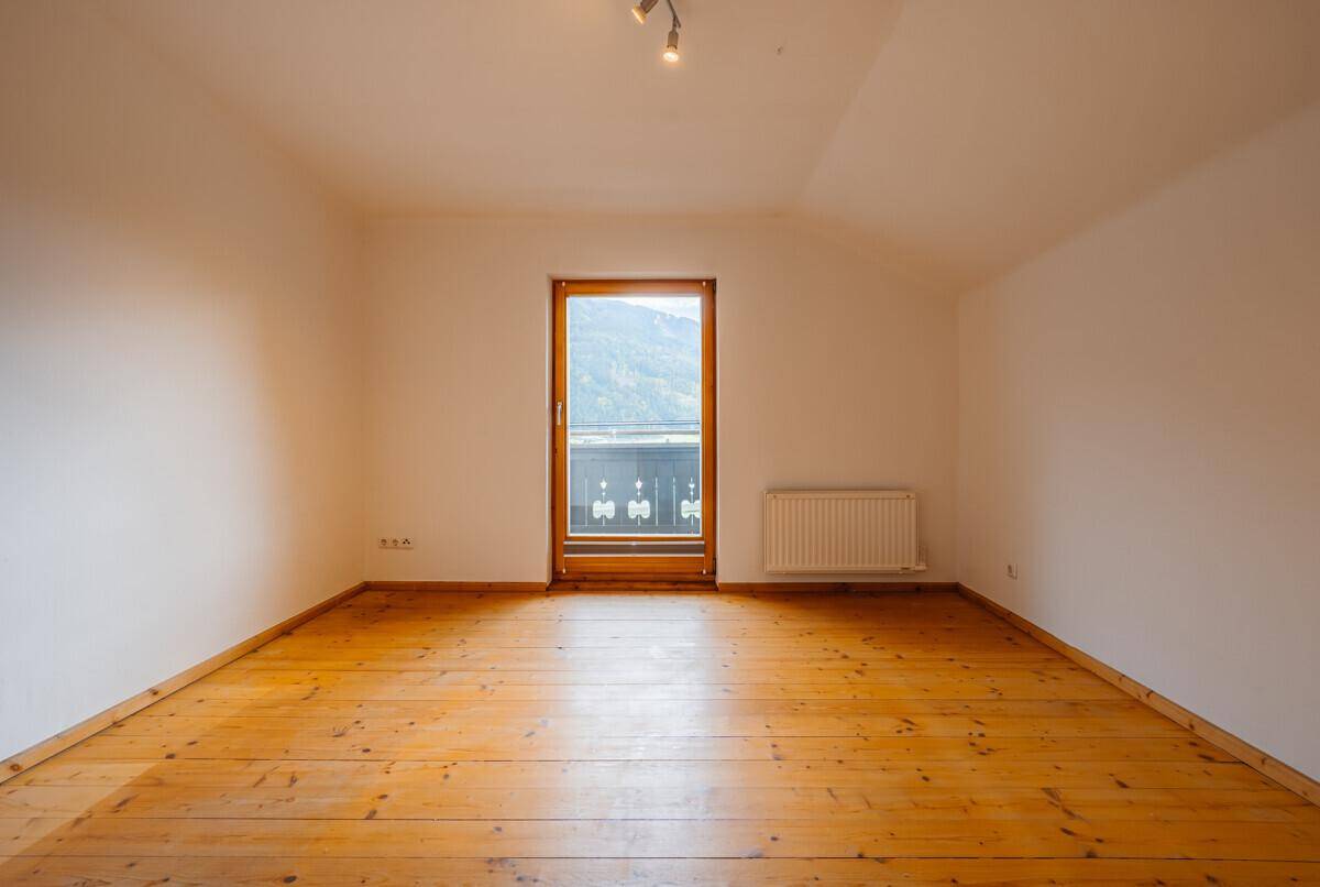 Geräumiges Zimmer mit Holzboden und Balkonzugang, der einen weiten Blick auf die Berge bietet.