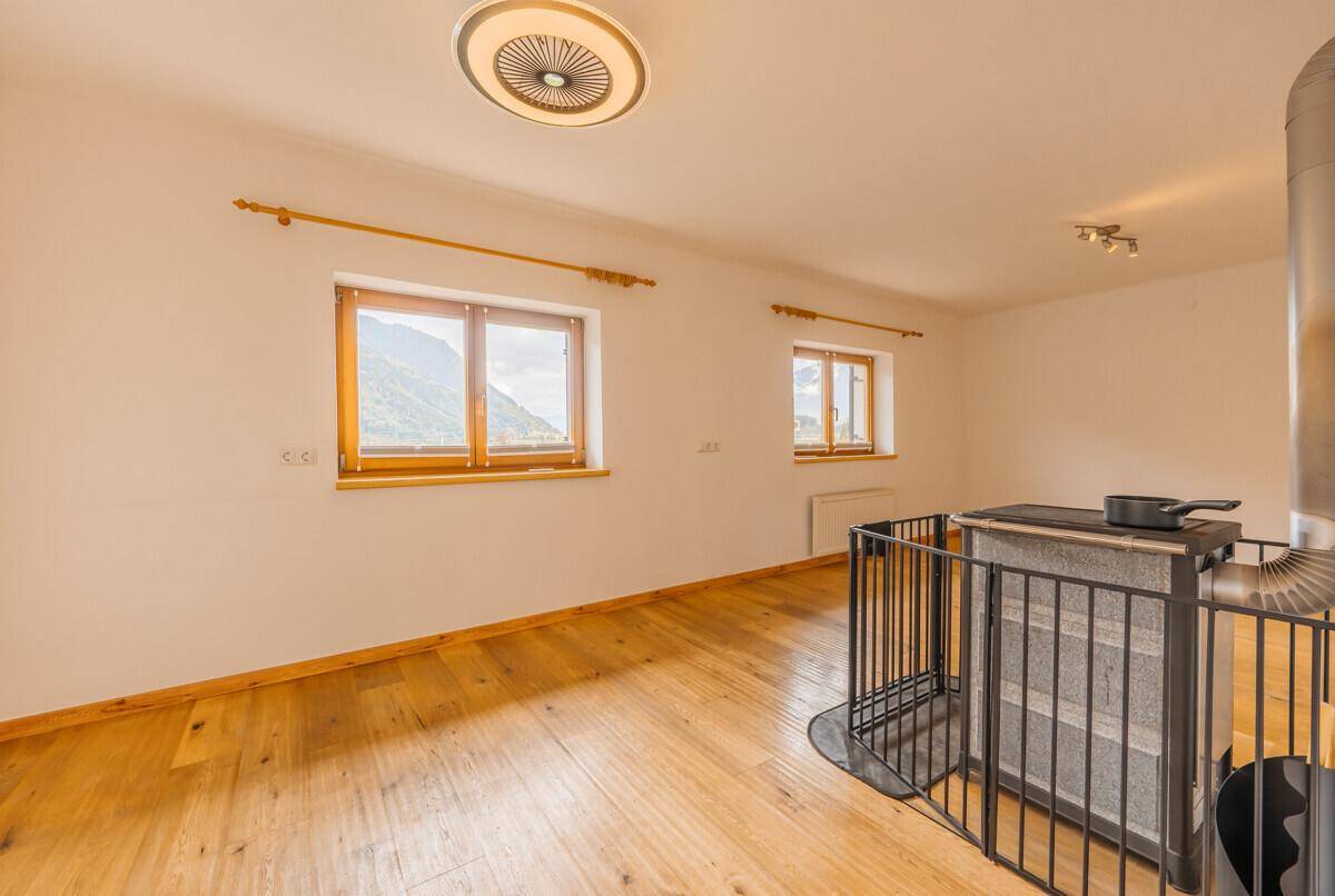 Helles Wohnzimmer mit Holzboden, einem gemütlichen Holzofen und Fenstern mit beeindruckendem Bergblick.