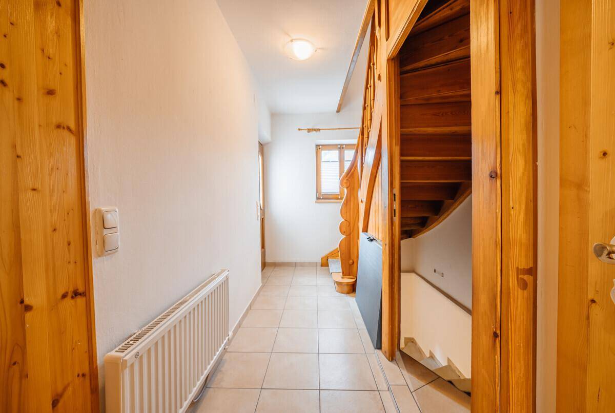 Heller Flur mit Fliesenboden, Holztreppe und Holztüren, der zu den oberen Etagen führt.