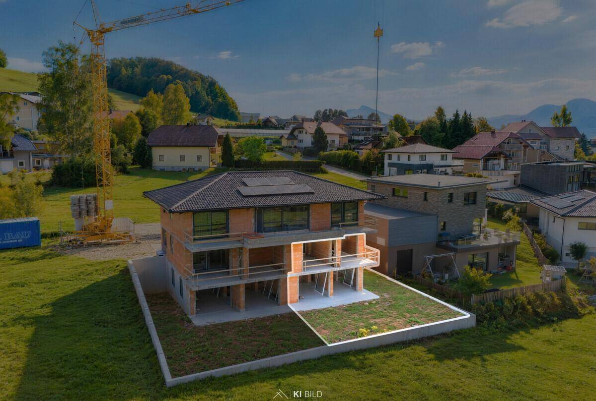 Neubau eines Mehrfamilienhauses im Rohbau mit hervorgehobener Balkonfläche und Bergblick.