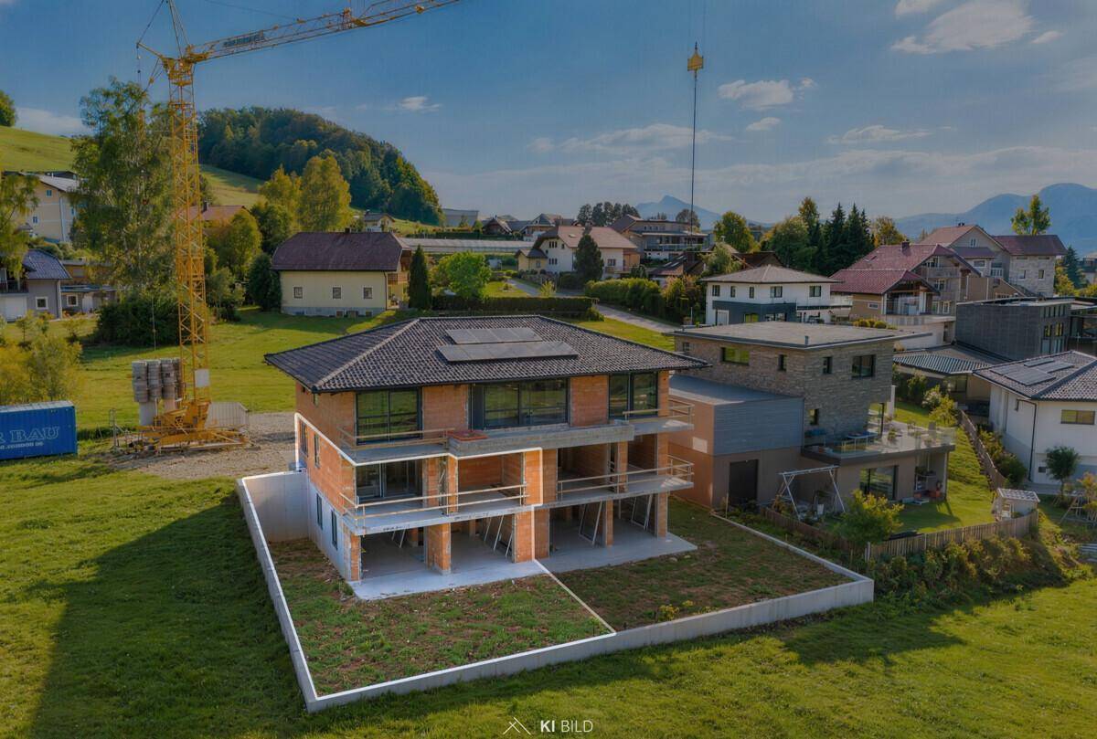Neubau im Rohbau mit markierter Grundstücksgrenze und Baukran in einer grünen Hügellandschaft.