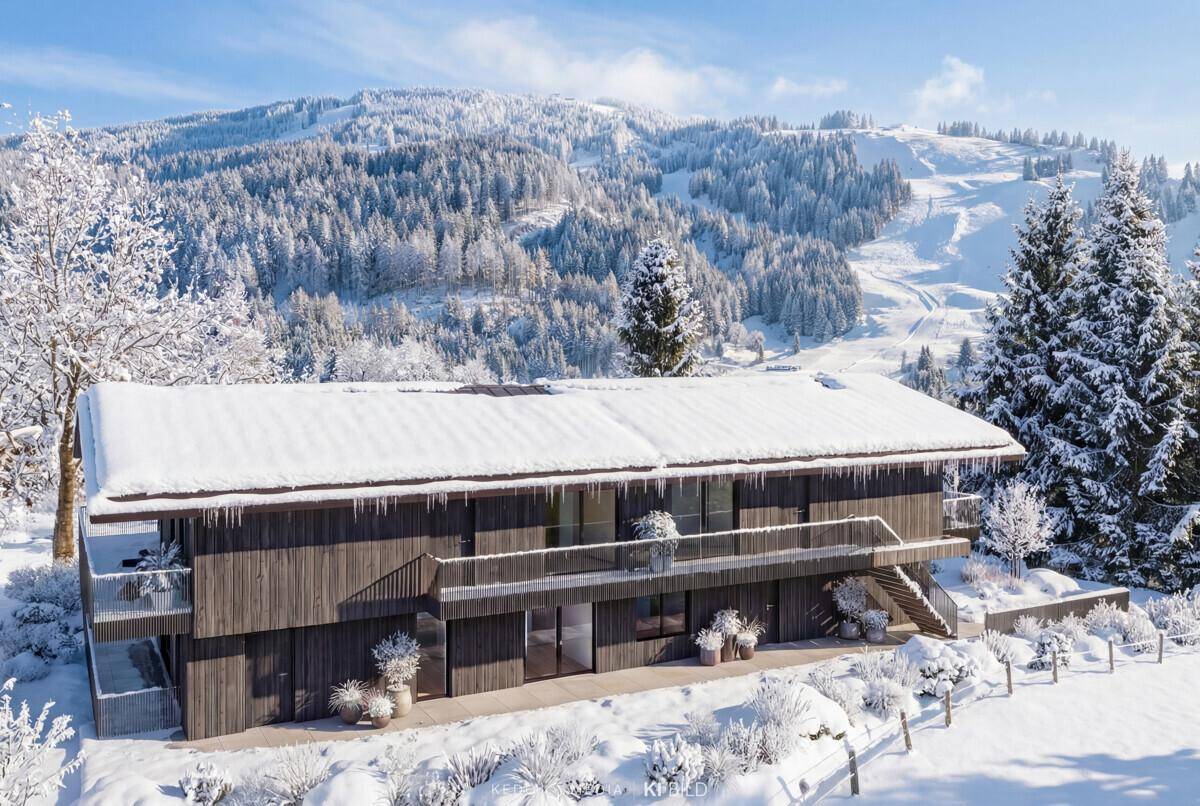 Moderne Holzfassade des Gebäudes mit Balkonen und Treppen, umgeben von verschneiter alpiner Landschaft.