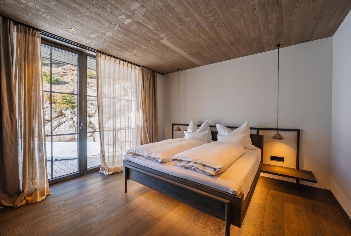 Helles Schlafzimmer mit Holzboden, Doppelbett und Zugang zu einem Außenbereich.