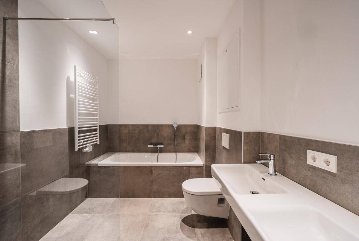 Modernes Badezimmer mit Badewanne, Wand-WC, Doppelwaschbecken und beheiztem Handtuchhalter.