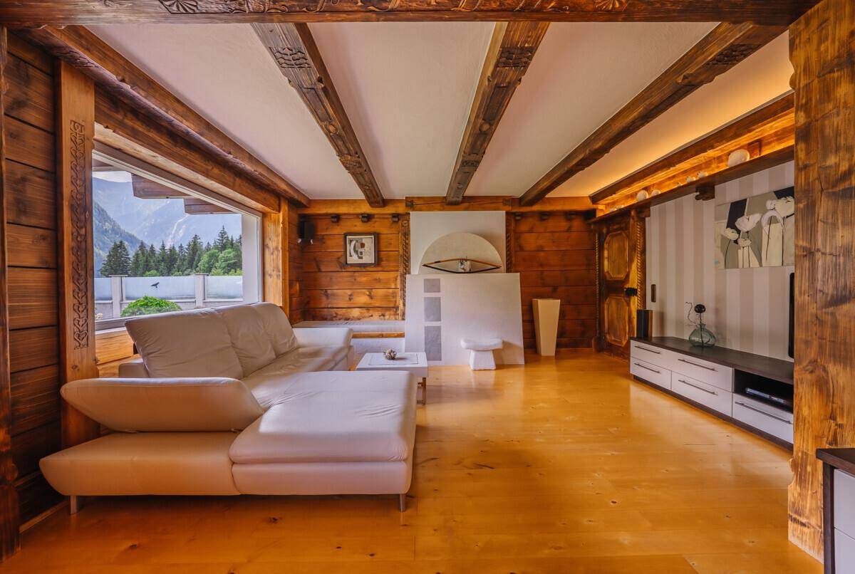 Rustikales Wohnzimmer mit Holzwänden, sichtbaren Balken und einem modernen Sofa.