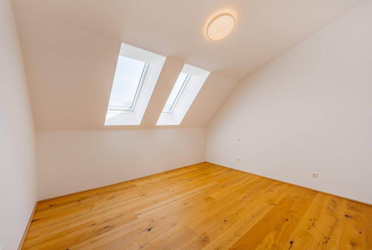 Helles Zimmer mit Holzboden, Dachschrägen und zwei Dachfenstern für viel Tageslicht.