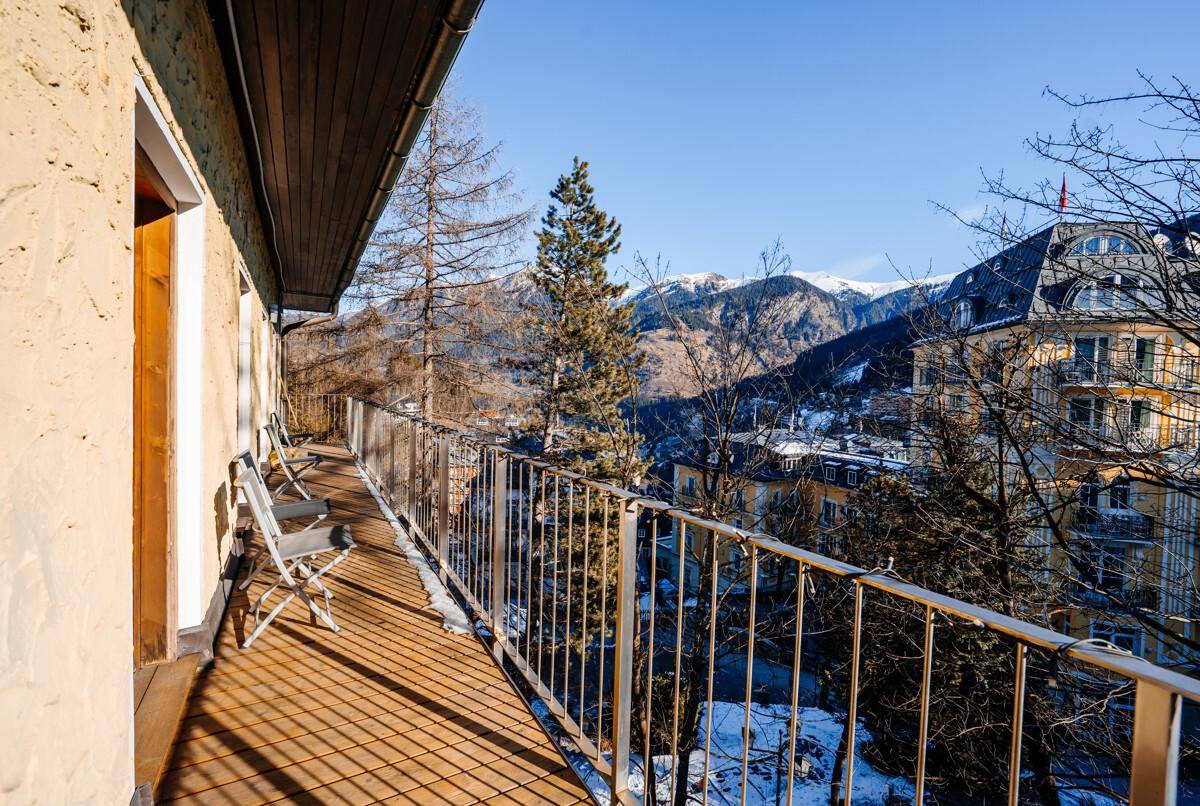 Langer Balkon mit Holzboden, Sitzgelegenheiten und weitem Blick auf die verschneite Bergwelt.